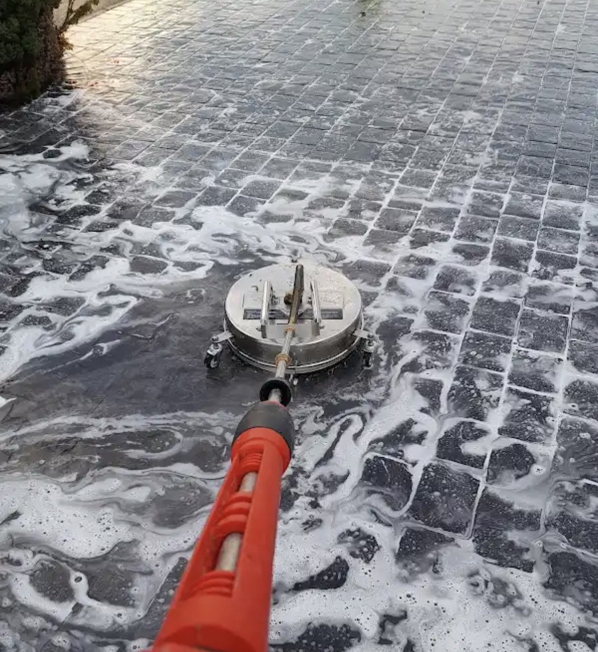 Rotary surface cleaner working across a foamed block-paved driveway
